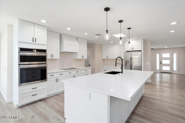 kitchen with custom exhaust hood, white cabinetry, appliances with stainless steel finishes, and sink