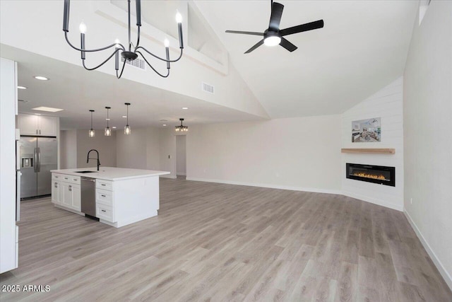 unfurnished living room featuring ceiling fan with notable chandelier, high vaulted ceiling, light hardwood / wood-style floors, and sink