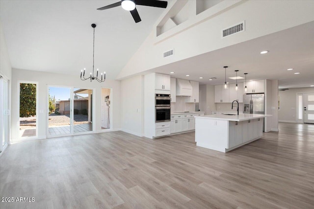 kitchen with sink, a kitchen island with sink, white cabinetry, stainless steel appliances, and decorative light fixtures