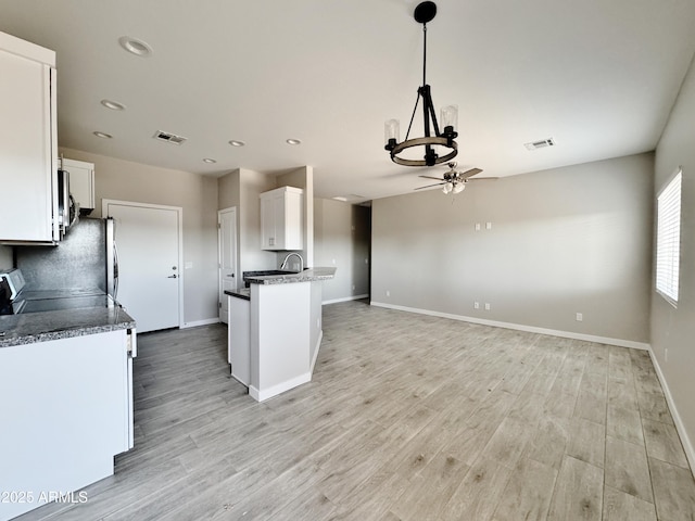 kitchen featuring stove, light wood-type flooring, ceiling fan with notable chandelier, pendant lighting, and white cabinets