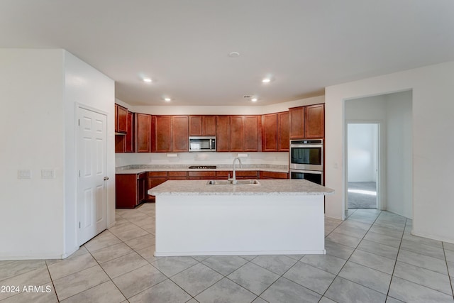 kitchen with a center island with sink, light tile patterned floors, sink, and appliances with stainless steel finishes