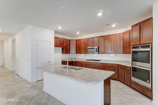 kitchen featuring appliances with stainless steel finishes, light tile patterned floors, sink, and a kitchen island with sink