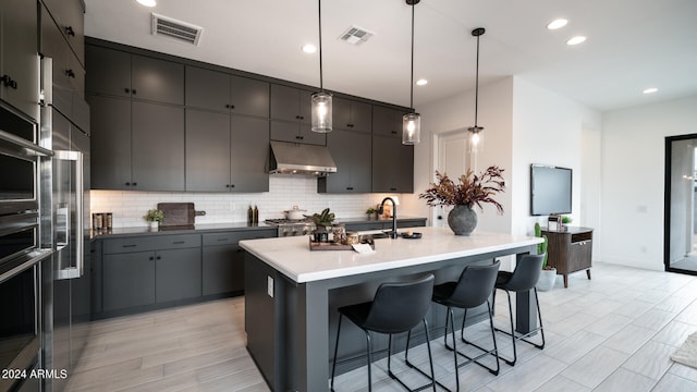 kitchen featuring gray cabinets, a center island with sink, hanging light fixtures, and decorative backsplash