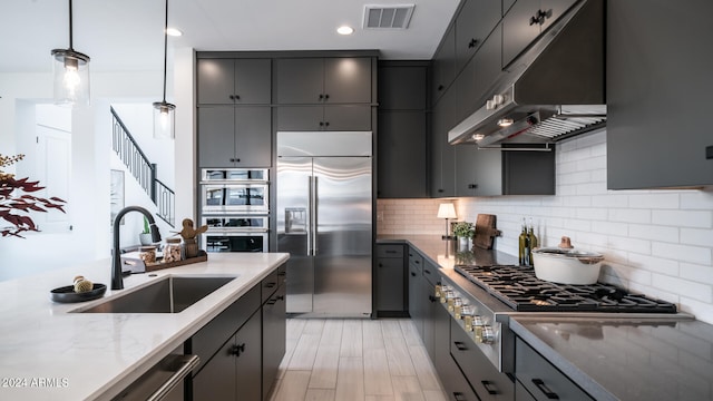 kitchen featuring pendant lighting, light hardwood / wood-style floors, tasteful backsplash, sink, and appliances with stainless steel finishes