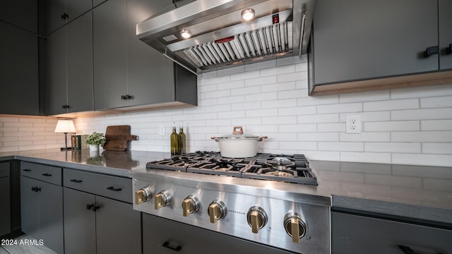 kitchen featuring decorative backsplash, stainless steel gas cooktop, wall chimney range hood, and gray cabinets