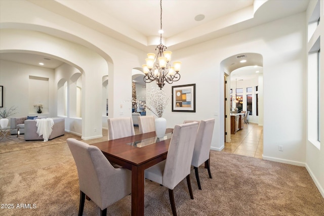 dining room featuring a tray ceiling, light carpet, light tile patterned floors, arched walkways, and a notable chandelier