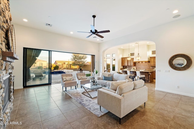 living room featuring visible vents, a ceiling fan, recessed lighting, arched walkways, and a stone fireplace