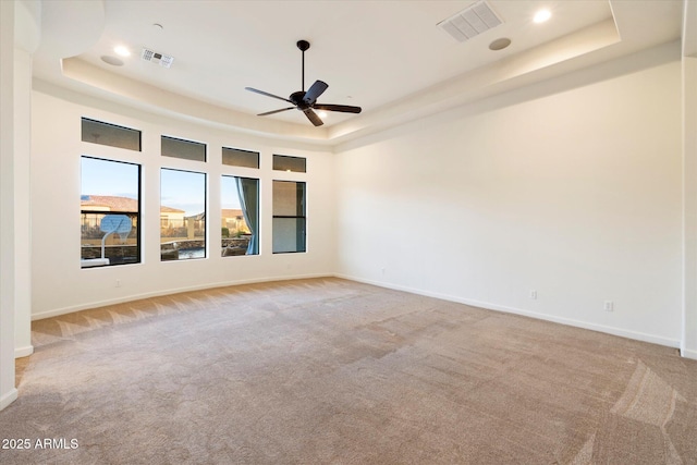 carpeted empty room with a tray ceiling, a ceiling fan, and visible vents