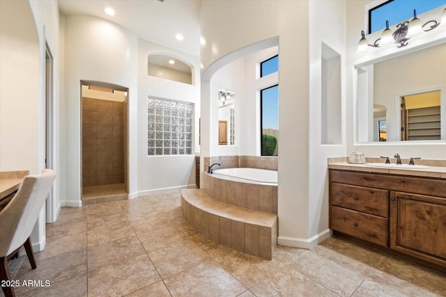 full bathroom featuring a garden tub, a walk in shower, baseboards, a towering ceiling, and vanity