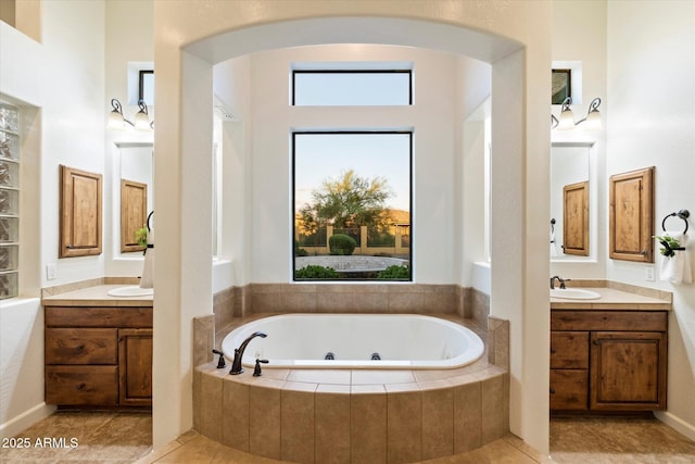 bathroom with tile patterned floors, a tub with jets, two vanities, and a sink
