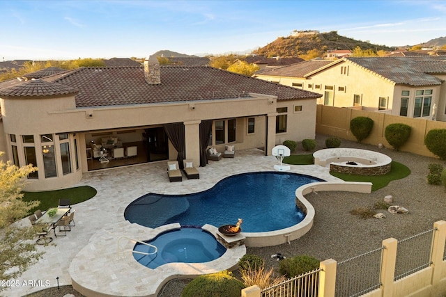 view of swimming pool with a pool with connected hot tub, a patio, a fenced backyard, an outdoor fire pit, and a mountain view
