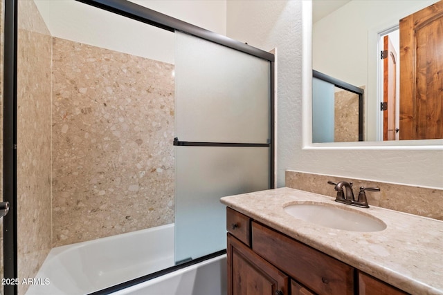 full bath with combined bath / shower with glass door, vanity, and a textured wall