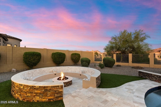 patio terrace at dusk with curved driveway, a fenced backyard, and an outdoor fire pit