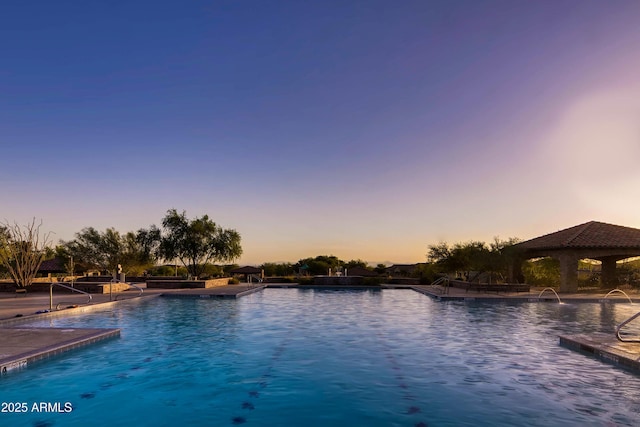 pool at dusk featuring a gazebo and a community pool