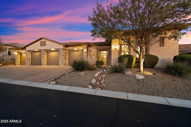 view of front of property with a tiled roof, stucco siding, a garage, stone siding, and driveway