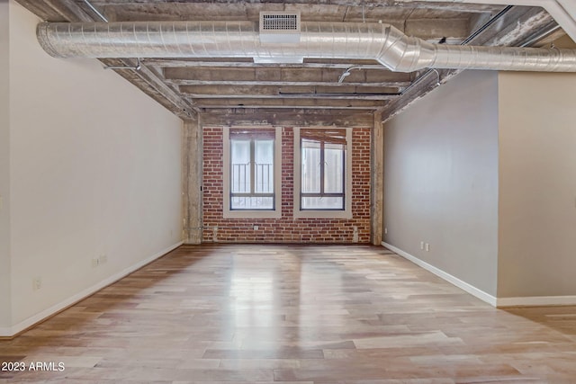 empty room with light hardwood / wood-style flooring and brick wall