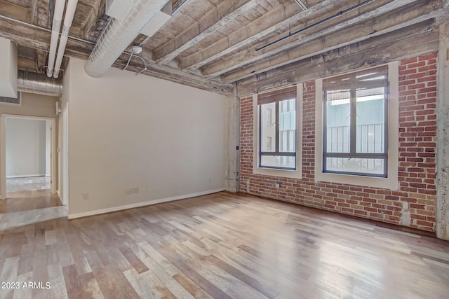 unfurnished room featuring light hardwood / wood-style floors, beam ceiling, and brick wall