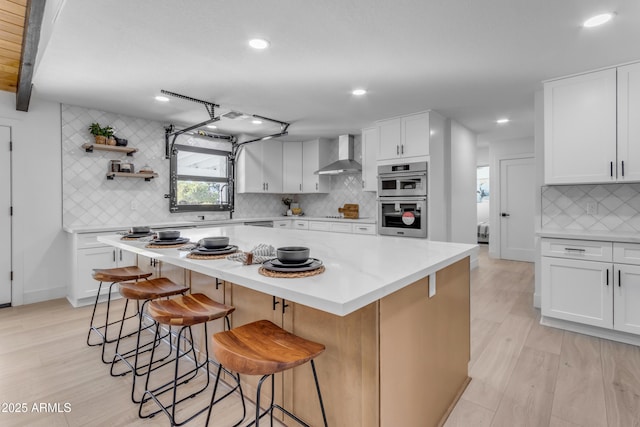 kitchen featuring a kitchen island, white cabinetry, stainless steel double oven, and wall chimney exhaust hood