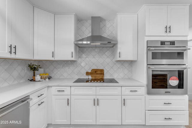 kitchen with appliances with stainless steel finishes, white cabinetry, decorative backsplash, and wall chimney exhaust hood