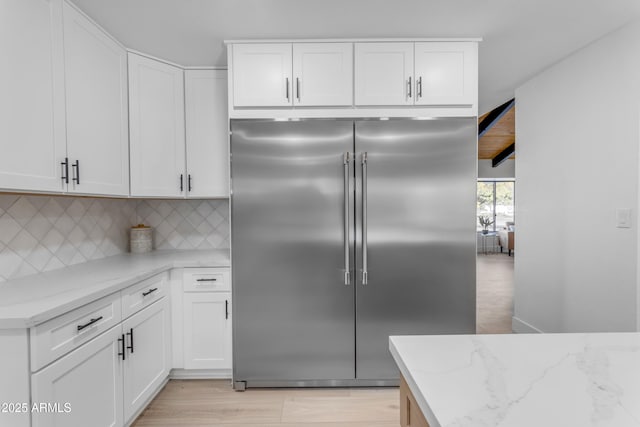 kitchen with light stone counters, white cabinets, stainless steel built in refrigerator, and tasteful backsplash