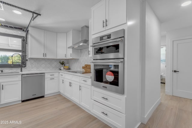 kitchen featuring stainless steel appliances, white cabinetry, and wall chimney exhaust hood