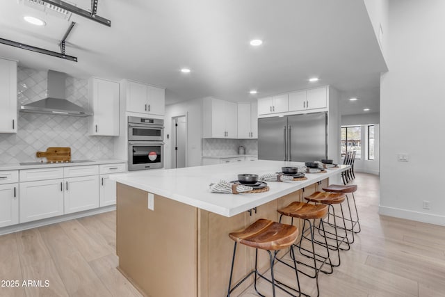 kitchen featuring appliances with stainless steel finishes, white cabinetry, a center island, and wall chimney exhaust hood