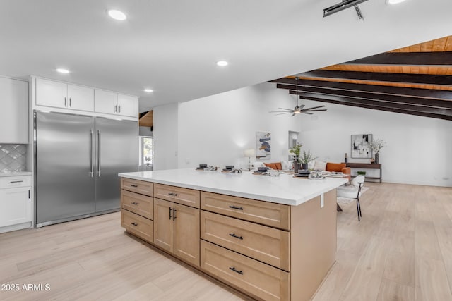 kitchen with lofted ceiling with beams, a center island, tasteful backsplash, built in fridge, and white cabinets