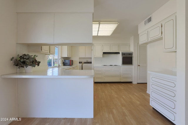 kitchen featuring white cooktop, light hardwood / wood-style flooring, independent washer and dryer, black oven, and kitchen peninsula