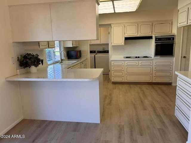 kitchen with light wood finished floors, a sink, black appliances, light countertops, and independent washer and dryer