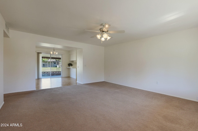 empty room featuring ceiling fan with notable chandelier and light carpet