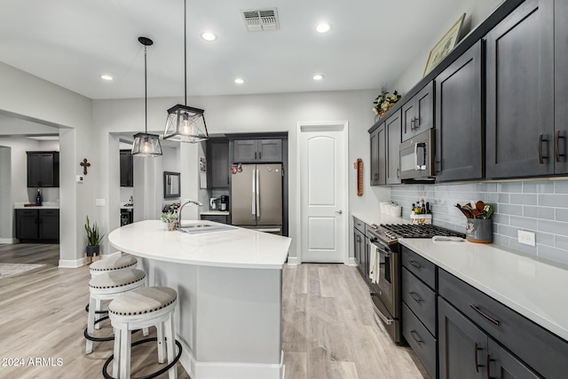 kitchen featuring sink, appliances with stainless steel finishes, hanging light fixtures, an island with sink, and light wood-type flooring