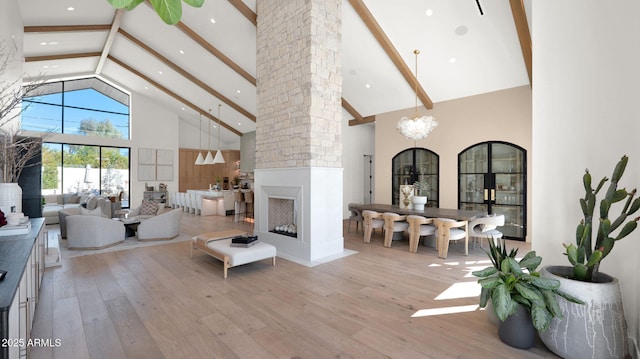 living room featuring beamed ceiling, high vaulted ceiling, a large fireplace, light wood-style floors, and a chandelier