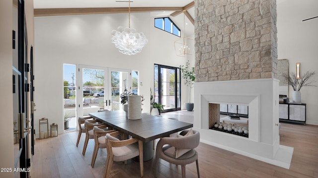 dining room with beam ceiling, a notable chandelier, a fireplace, and wood finished floors