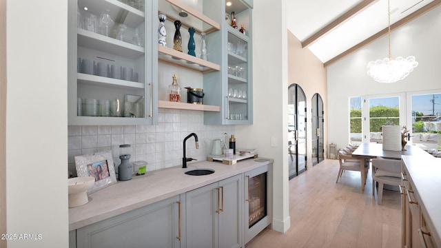 kitchen featuring tasteful backsplash, wine cooler, light countertops, light wood-type flooring, and a sink