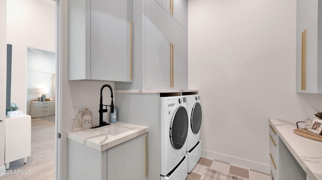 clothes washing area with a sink, baseboards, cabinet space, and washing machine and clothes dryer