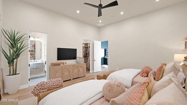 bedroom featuring light wood-style flooring, a high ceiling, recessed lighting, a walk in closet, and connected bathroom