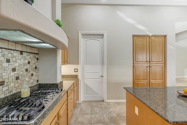 kitchen with range hood, stainless steel gas stovetop, dark stone counters, and tasteful backsplash