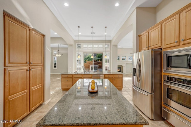 kitchen with dark stone counters, a sink, a kitchen island, appliances with stainless steel finishes, and a warming drawer