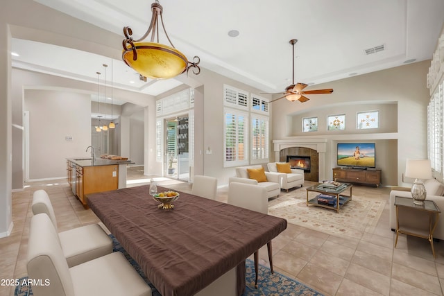 dining space featuring a raised ceiling, visible vents, a glass covered fireplace, light tile patterned flooring, and baseboards