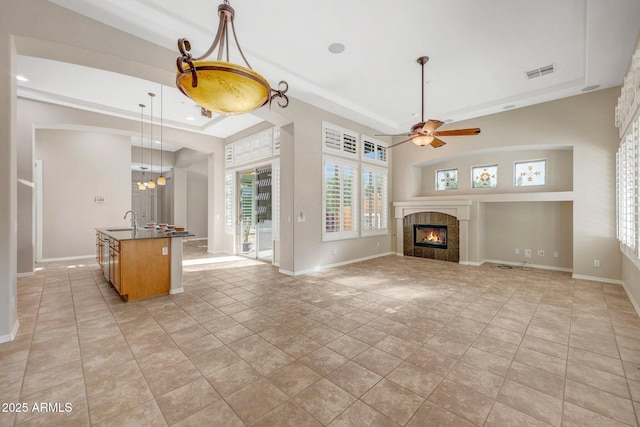 unfurnished living room with a sink, visible vents, baseboards, a tray ceiling, and a tiled fireplace