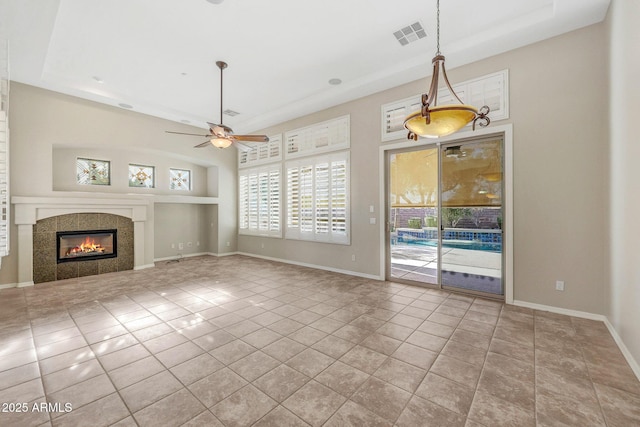 unfurnished living room with visible vents, a ceiling fan, a tile fireplace, baseboards, and tile patterned floors