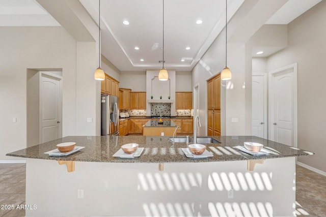 kitchen with stainless steel refrigerator with ice dispenser, a breakfast bar area, backsplash, a sink, and a large island with sink