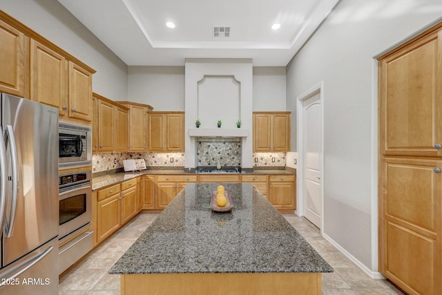 kitchen with stainless steel appliances, a kitchen island, dark stone counters, a tray ceiling, and tasteful backsplash