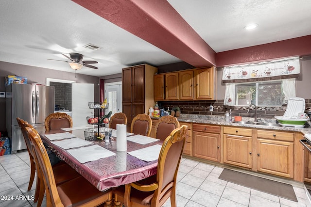 kitchen with sink, ceiling fan, light stone countertops, light tile patterned floors, and stainless steel refrigerator