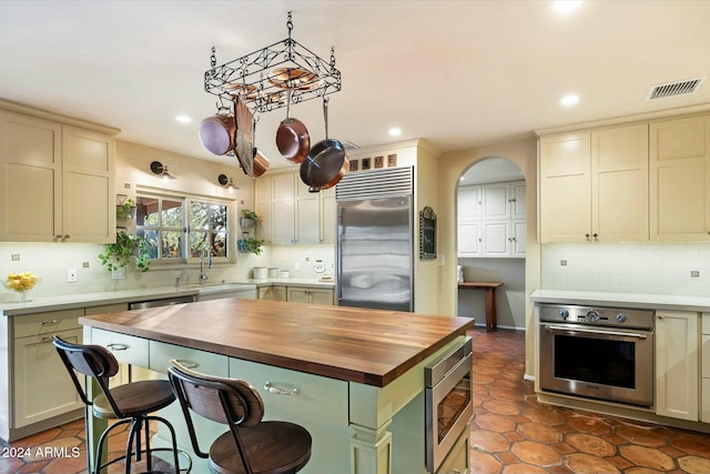 kitchen featuring sink, wood counters, built in appliances, cream cabinets, and a kitchen island