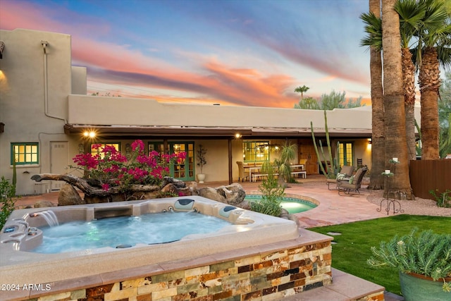 pool at dusk with a patio and a hot tub