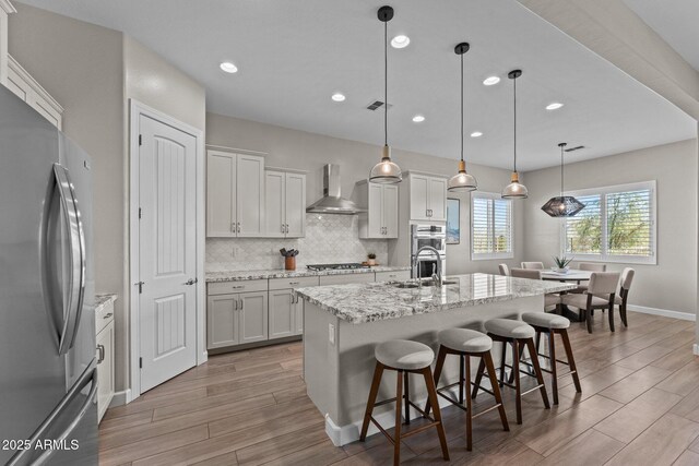 kitchen with stainless steel appliances, backsplash, wood tiled floor, wall chimney range hood, and a kitchen bar