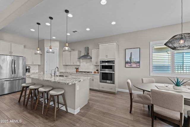 kitchen featuring a sink, appliances with stainless steel finishes, wall chimney range hood, and tasteful backsplash