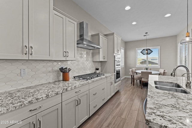 kitchen with stainless steel appliances, wood finished floors, a sink, backsplash, and wall chimney exhaust hood