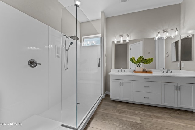 bathroom with wood finished floors, double vanity, a sink, and a walk in shower